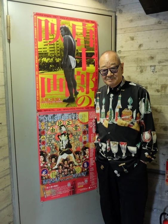 男性が唐十郎関連のポスターの前に立つ画像