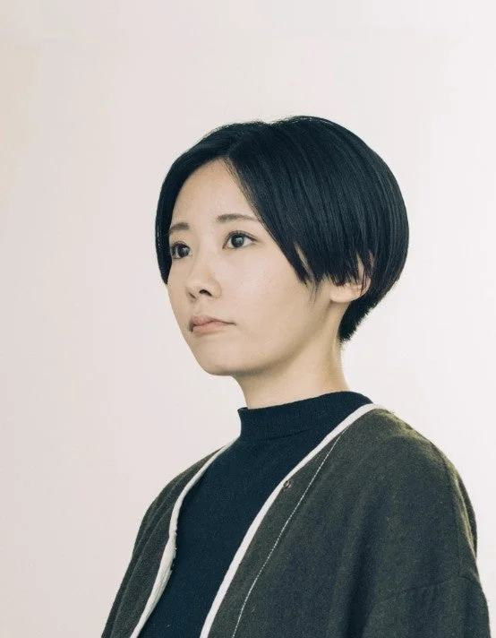 白いシンプルな背景を背に、ショートヘアの若い日本人女性が左方向を見つめているポートレート