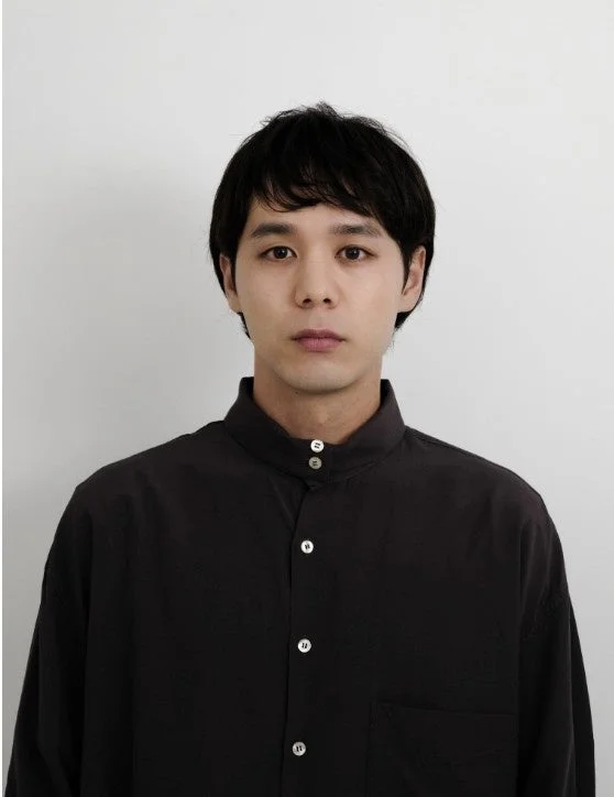 白い背景を背に、黒いスタンドカラーシャツを着た若いアジア人男性のポートレート写真