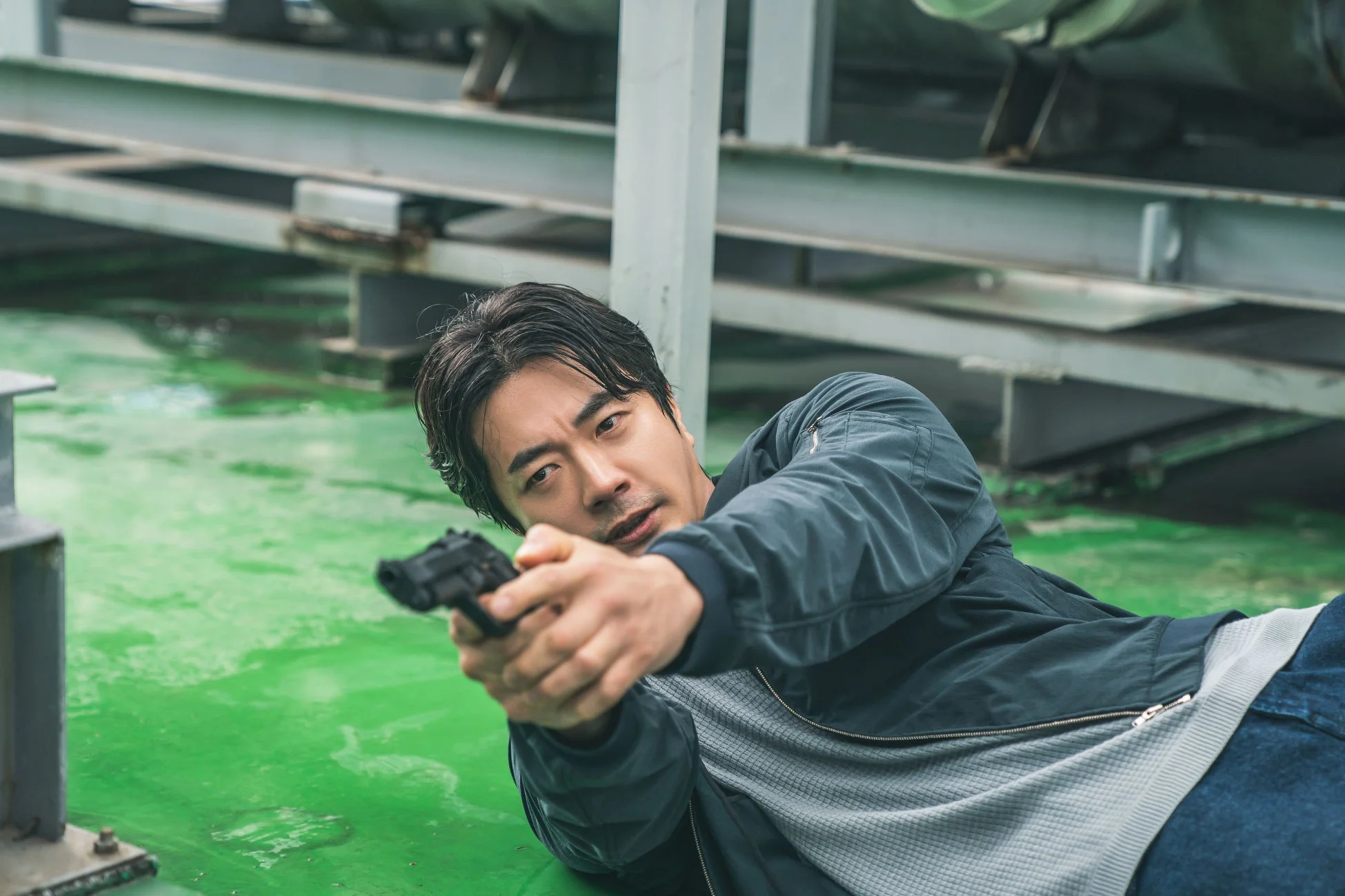 緑色の床に伏せ、銃を構える男性の姿。緊迫した状況下で標的を狙っている様子が伺える。